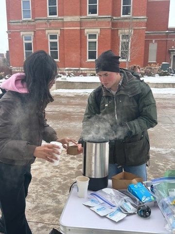 OUR Ambassador handing out hot chocolate to a student learning about research!